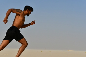 Runner on the sand in desert: Young adult man, is running on the sand hill in desert area and he is enjoying the sand and sunlight. His slim body suggests that he is a fitness model working out daily to maintain a healthy life style and healthy living habits.